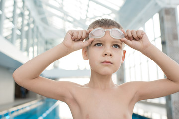Serious determined male kid looking into distance and preparing for training in swimming pool, he adjusting goggles