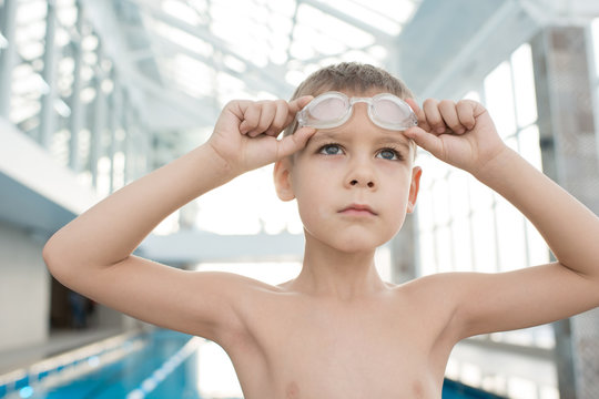 Serious determined male kid looking into distance and preparing for training in swimming pool, he adjusting goggles