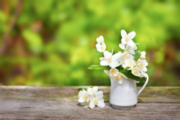Fototapeta na wymiar Delicate jasmine flowers in vase on old wooden board, green blurred background