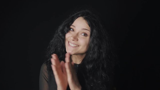 portrait of cheerful woman with curly hair and brown eyes claps and laughs at black background