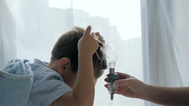 aching child breathes through an inhaler for treatment difficulty breathing in hospital