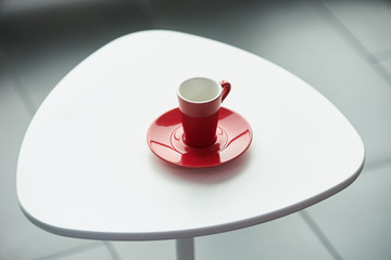 Red cup for tea or coffee on a white triangular bar table in coffee shop interior