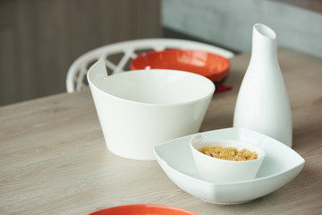 Ceramic bowl with raw fusilli pasta and white dishes on kitchen table, close-up.
