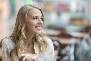 Pretty smiling blonde starting in a cafe with a cup of a fresh brewd coffee