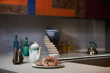 Morning breakfast on a ceramic tray in the modern kitchen interior. Kettle, coffee pot, cup of tea, napkins and croissant on kitchen counter