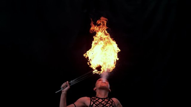 Fire artist entertainer breathes burning flame in the dark