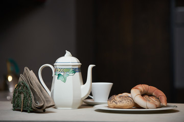Morning breakfast on a ceramic tray in the modern kitchen interior. Kettle, coffee pot, cup of tea, napkins and croissant on kitchen counter