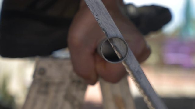A craftsman sawing a piece of steel pipe