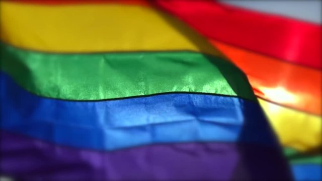 Gay pride rainbow flag flying in backlit close-up