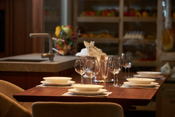 Luxury kitchen dining table setting, glasses, cutlery and wine in ice bucket. Modern kitchen interior with clean white plates, glasses and cutlery on wooden table