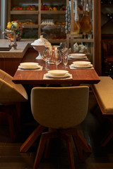 Luxury kitchen dining table setting, glasses, cutlery and wine in ice bucket. Modern kitchen interior with clean white plates, glasses and cutlery on wooden table