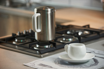 Coffee pot on gas stove and cup of coffee on modern kitchen counter table, close-up. Morning breakfast with hot coffee