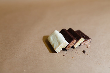 Four chocolate protein bars with different flavors in the context of sprinkle rice flakes on baking paper, Teflon paper. Whey protein powder and chocolate protein bar on wooden background. Text space
