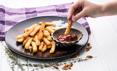 Childs hand dipping a potato chip into tomato ketchup Portion of french potatoes on white wooden background.