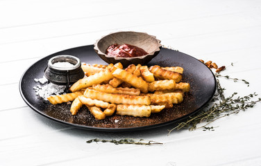 French potatoes on black plate with bowl of ketchup and sea salt. White wooden table.