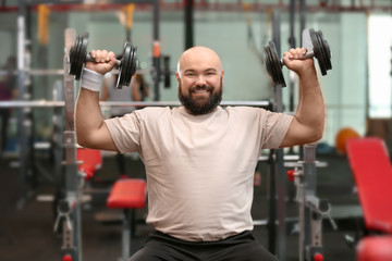 Overweight man training with dumbbells in gym