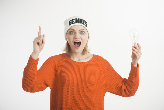 Idea And Creative Concept. Woman Points Up With Finger, Has Idea, White Background. Lady In Hat With Genius Word, Found Out Idea. Lady With Shocked Face Holds Lamp In Hand, Symbol Of Idea.