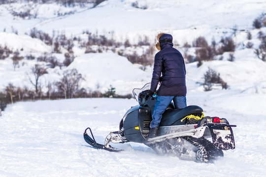 Man rides on snowmobile in standing position through snowy fields. Winter adventures