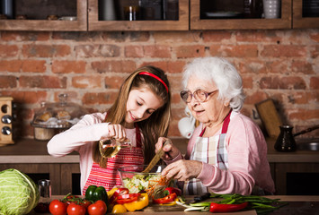Grandmother and cute granddaughter cooking healthy food at home at kitchen