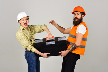 Builders with toolbox, couple in love makes repair grey background. Renovation concept. Smiling woman in helmet excited about renovation. Repairman and girlfriend holding toolbox together, copy space.