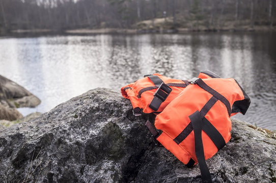 Orange life jacket lies on the rocky shore of the lake in the background, cloudy day in early spring.