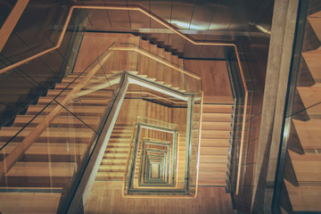 Spiral staircase from above with parquette floor. Square shaped stairs going downwards creating...