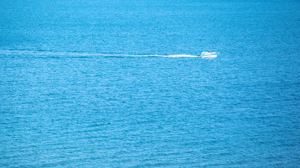 a small solitary white yacht sails in the middle of the blue sea