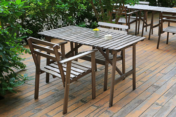 Vintage style wooden table and chair in the garden with glass of flower decoration and ceramic cigarette ashtray.