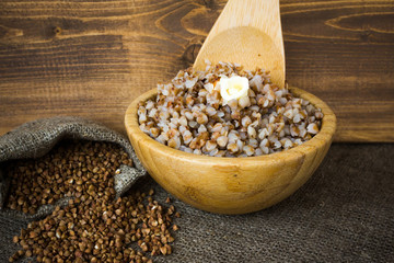 Boiled buckwheat groats in bowl with butter, a baggie of dry cereal. Wooden background.