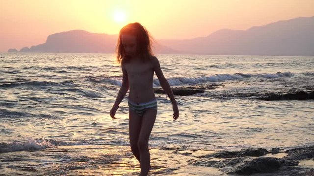 A cute and funny children runs on the water, the boy and girl are on the nature near a sea, strong wind and waves on sunset
