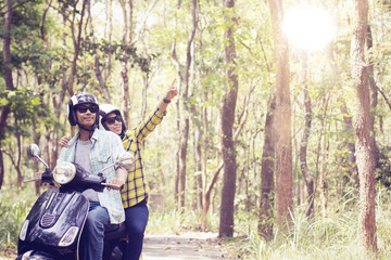 Beautiful young couple in helmets riding a scooter through forest. life style idea concept