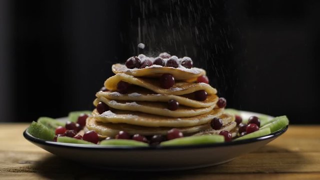 American breakfast pancakes served at the restaurant. Pancakes pile on plate decorated with berries and kiwi dusted with powdered sugar, isolated. Slow motion