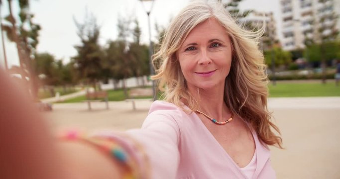 Beautiful senior woman taking selfies on a smartphone in park