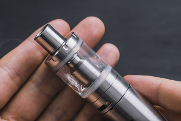 Man hand shows vape device at cloud of vapor background. Vape concept, toned
