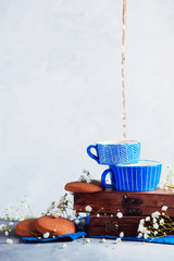 Cookies in a morning scene on a light background with copy space. Breakfast concept with homemade pastry and spring gypsophila flowers. Blue ceramic teacup with wooden boxes.