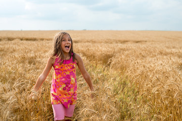Happy little girl in a field of ripe wheat