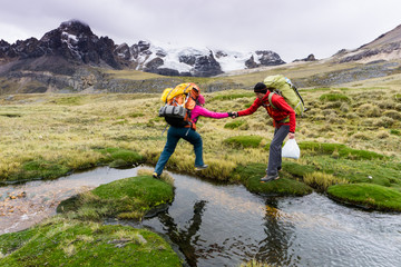 male mountain climber helps his female partner cross a small mountain stream high up in the Cordillera Blanca in the Andes in Peru
