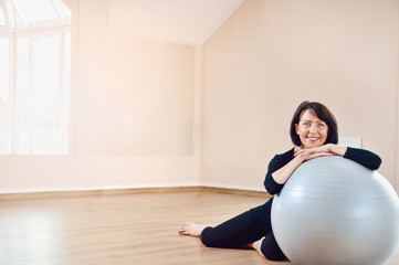 Happy senior woman resting after exercise with gray exercise ball