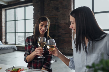 Two cheerful friends having dinner drinking wine home