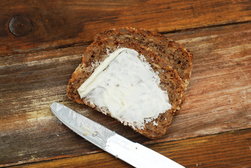 Slices of Homemade Whole Grain Bread with Butter and Knife over Wooden Background with Copy Space.