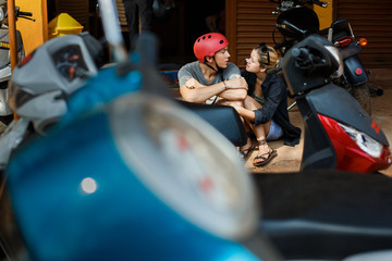 Fototapeta na wymiar A guy and a girl are sitting on the ground next to a garage repair shop for motorbikes