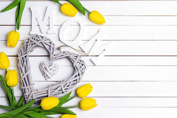 Mothers day background with decorative heart and yellow tulips on white wooden table.