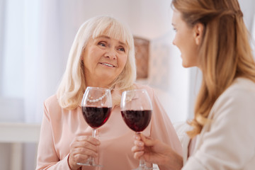 Family time. Nice joyful aged woman holding a glass of wine and looking at her daughter while having a celebration with her
