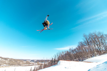 skier in the sky grabbing the back of his ski with a blue sky background  high up in the air