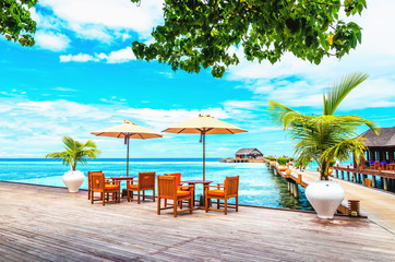 Fototapety  Restaurant with sun umbrellas on a wooden pier against the azure water of the ocean