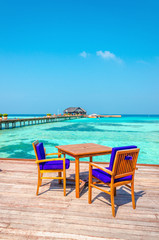 Tables and chairs in a wooden restaurant on stilts on the background of azure water and sunny sky