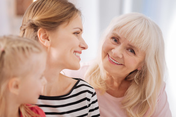 Family members. Happy joyful elderly woman sitting together with her family members and smiling to you while being in a great mood