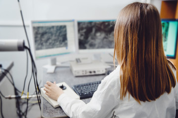 Back view. Young female student is an engineer working on computers, analyzing data obtained during experiment.
