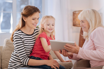 Family meeting. Pleasant happy cheerful family smiling and looking at the tablet while spending time together