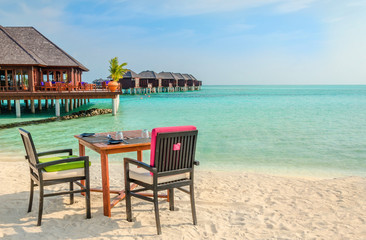 Table and chairs at restaurant at the background of water bungalows, Maldives